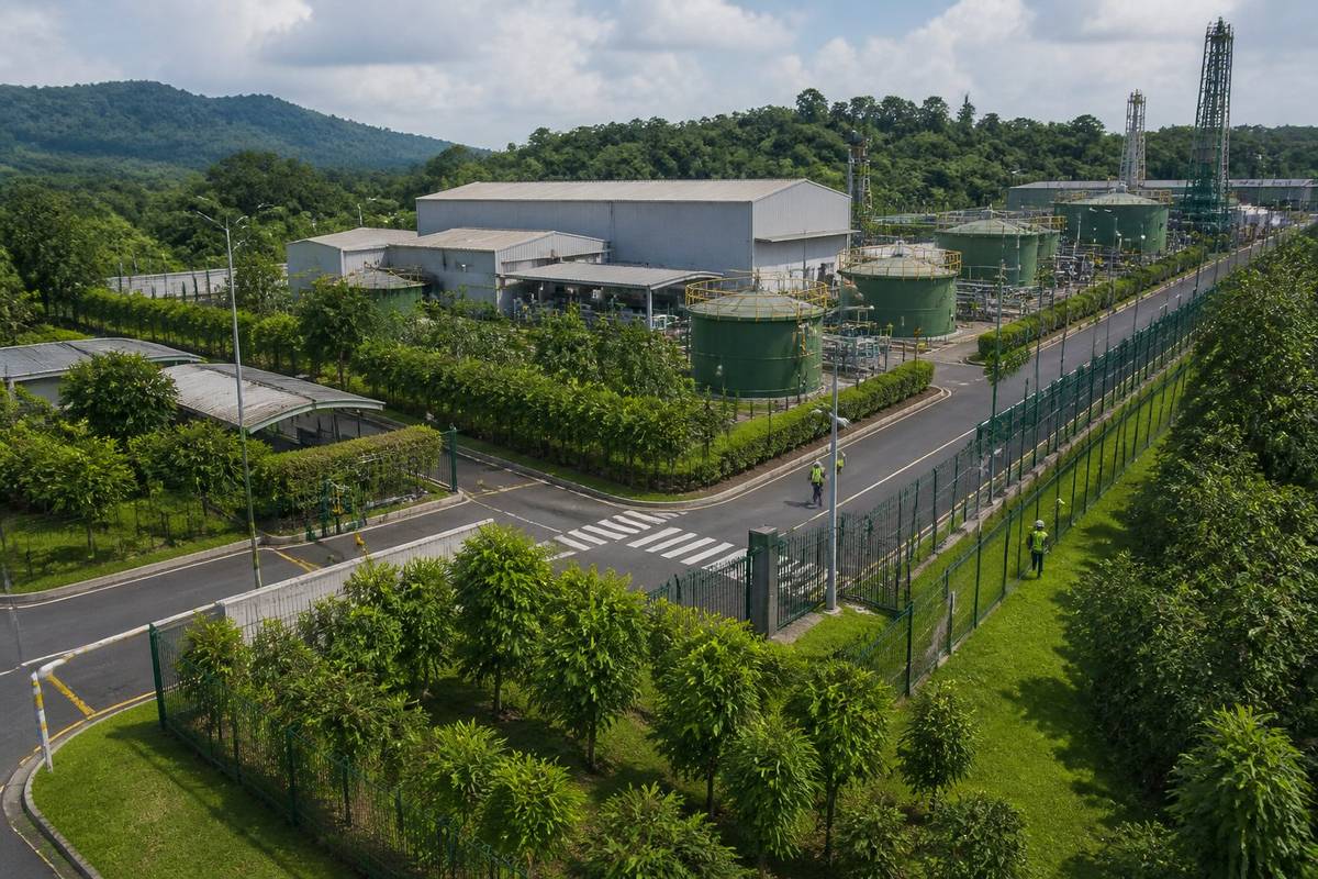 Área industrial cercada e monitorada, com instalações modernas e uma faixa de vegetação preservada ao redor.